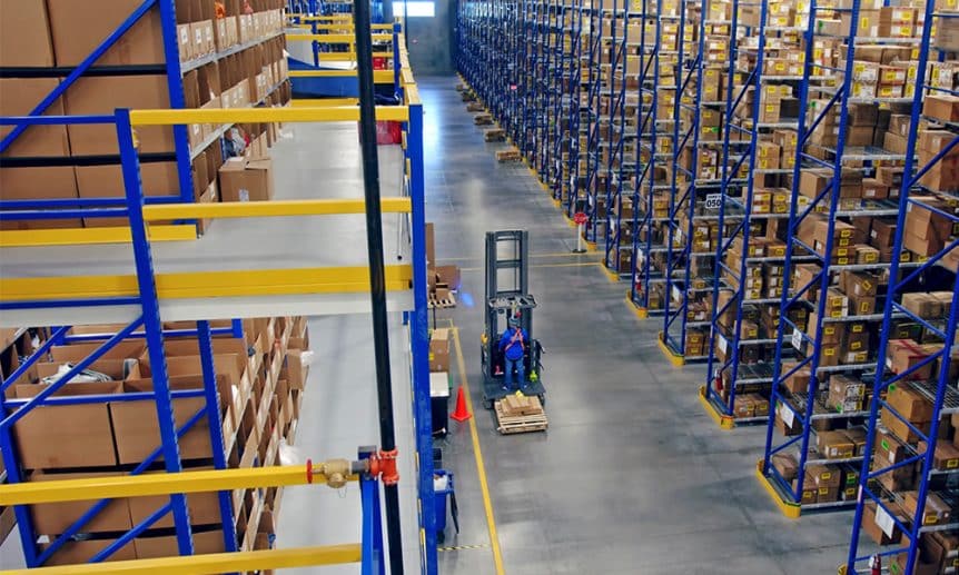 Man on a narrow aisle forklift in between pallet rack aisles in a warehouse